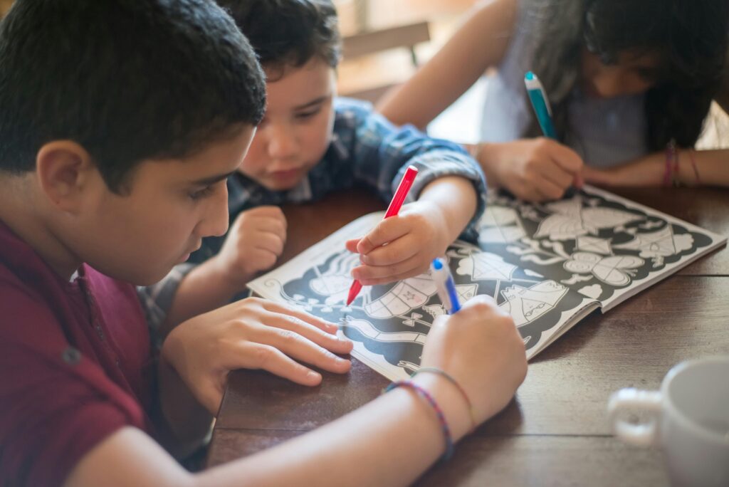 A group of children focused on coloring in an activity book at a wooden table.